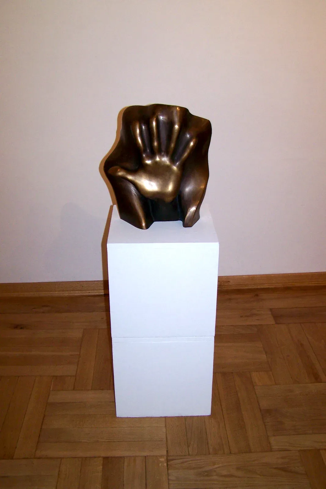 Il bronzo su un plinto bianco al centro di una sala dalle pareti chiare e dal parquet a spina, visto di fronte e a figura intera