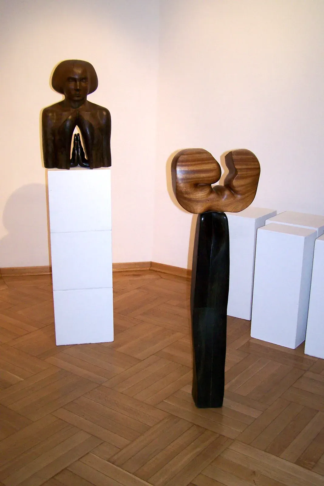 Skupienie — Il busto su un plinto alto, in una sala dal parquet a spina; accanto, un’altra scultura di legno su base scura.