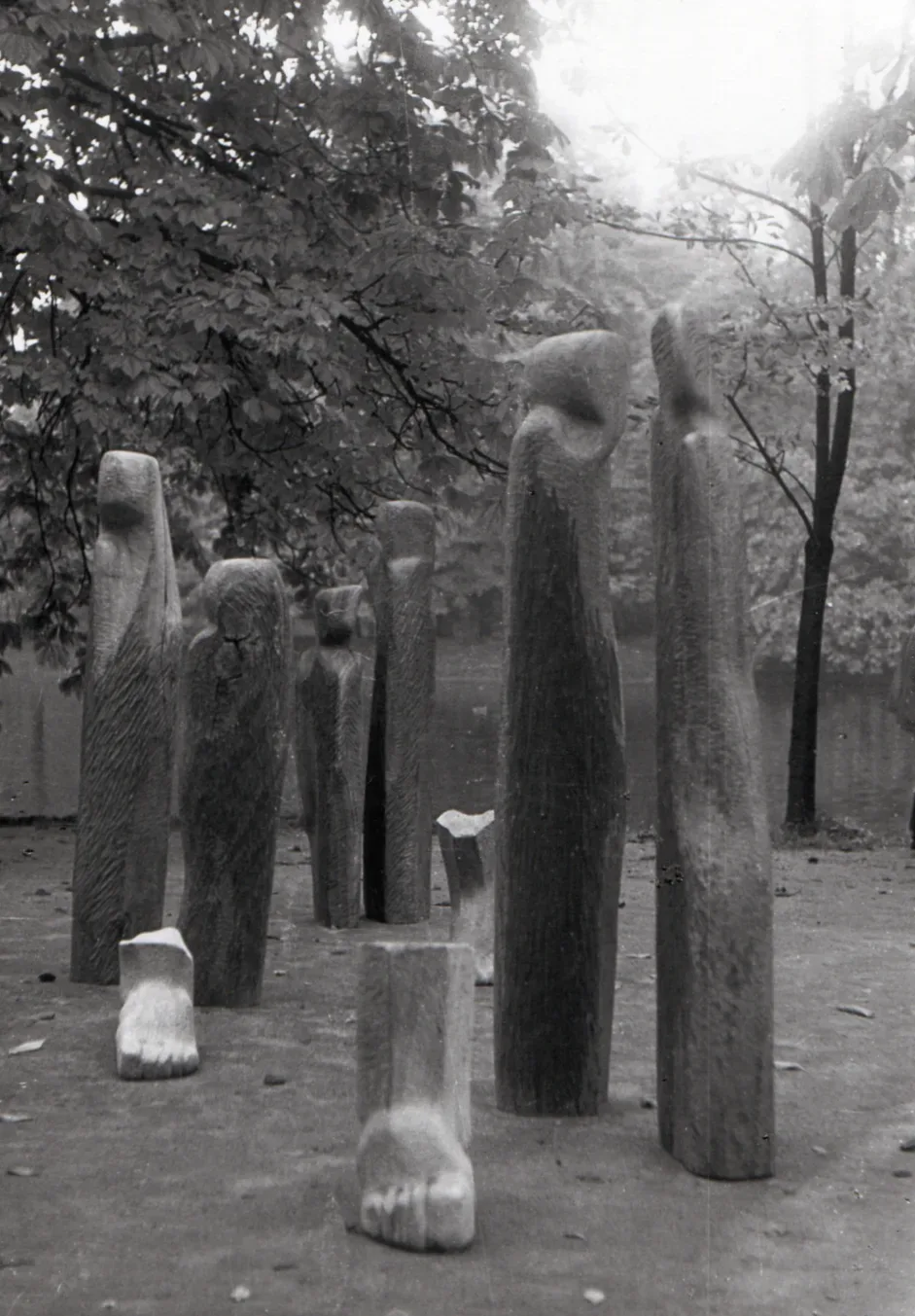 Wygnanie: dieci figure in mogano tra gli alberi, con piedi scolpiti a terra in primo piano