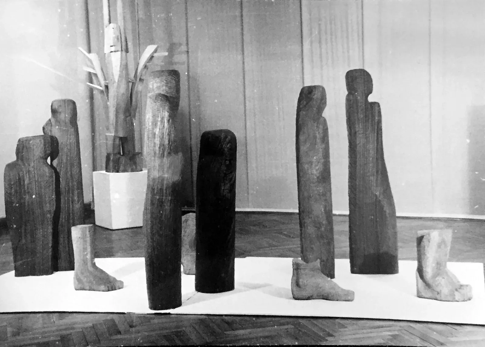 Wygnanie — Stampa d’epoca: il gruppo su una pedana bassa in una sala dal parquet a spina, davanti a un fondale di tendaggi chiari. Si contano tutti e dieci gli elementi — sei figure e quattro piedi.