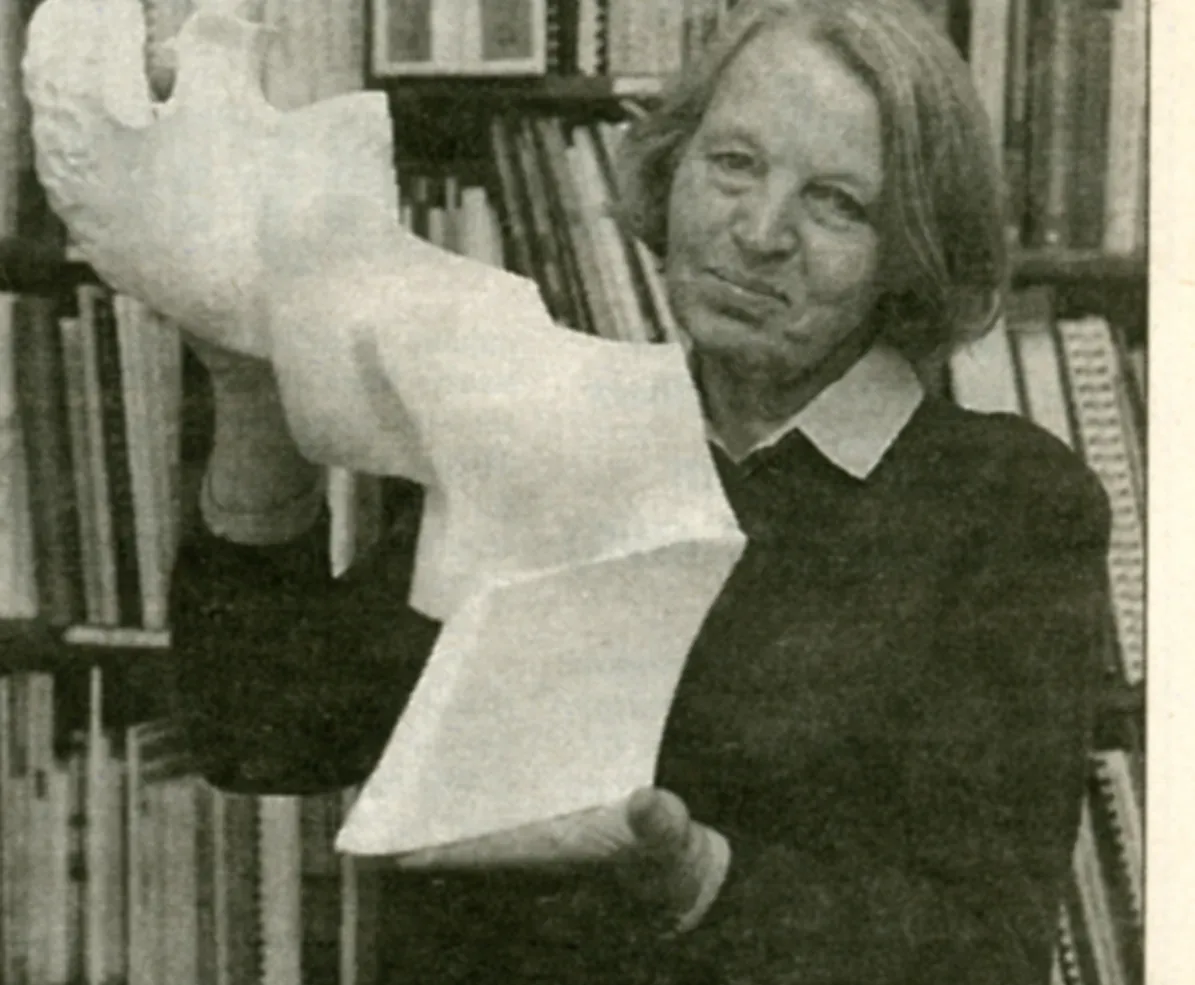 Fotografia di giornale: Antonina Wysocka-Jonczak regge in alto il modello in gesso del monumento davanti agli scaffali della libreria dello studio