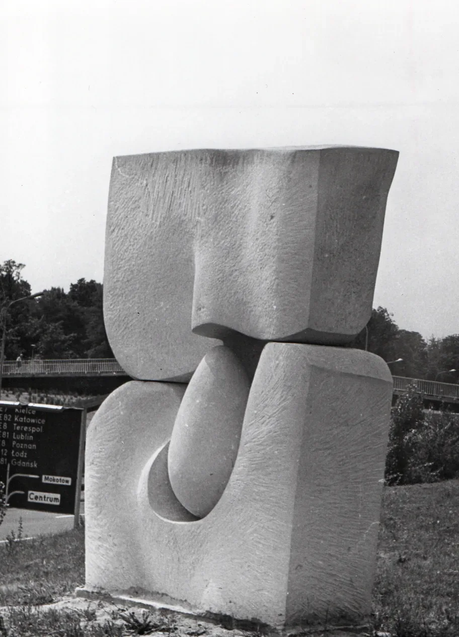 La stessa scultura ripresa dalla scarpata, di taglio: dietro di lei il cartello stradale con l’elenco delle città e il viadotto della strada