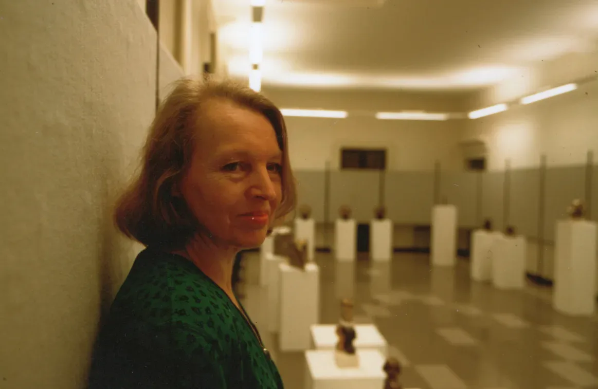 Antonina appoggiata a una parete in una galleria, con le sue sculture da camera su plinti bianchi sullo sfondo