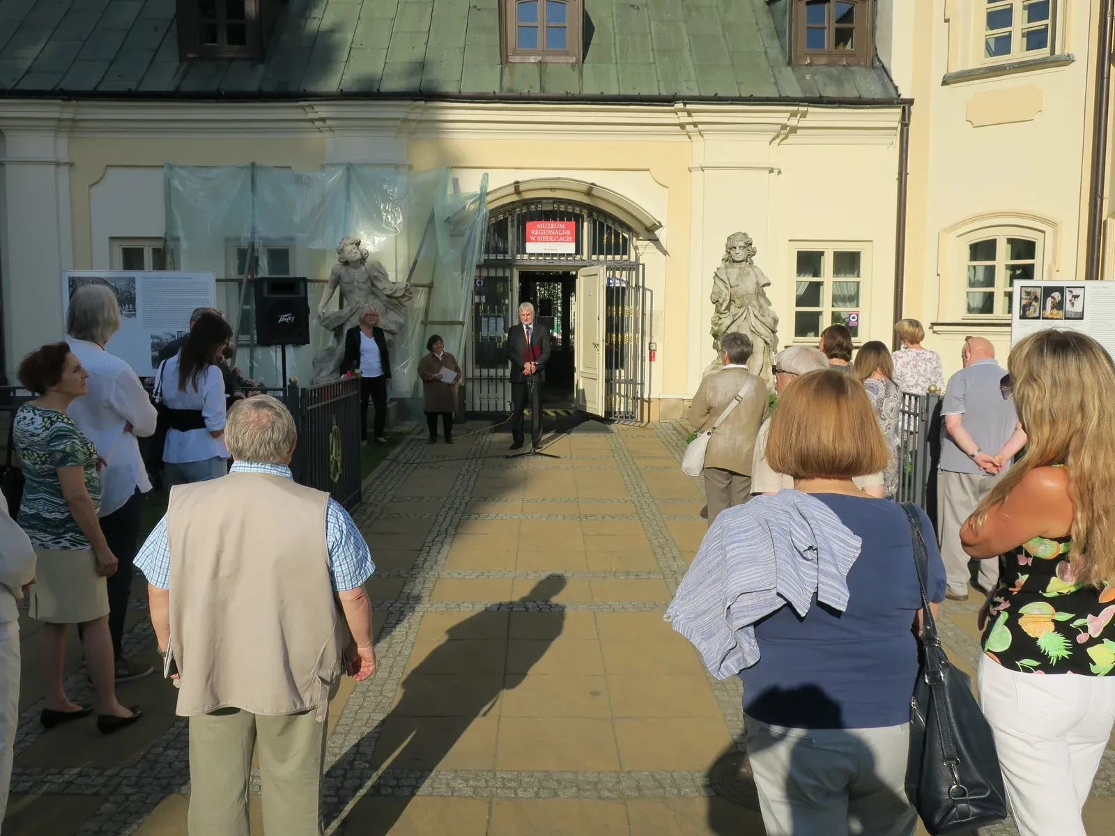 Inaugurazione all’aperto davanti al museo di Siedlce: un oratore parla al microfono davanti al portale, il pubblico ascolta in piedi.